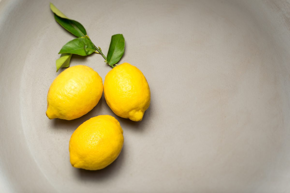 Three lemons and leaves in a shallow stoneware bowl