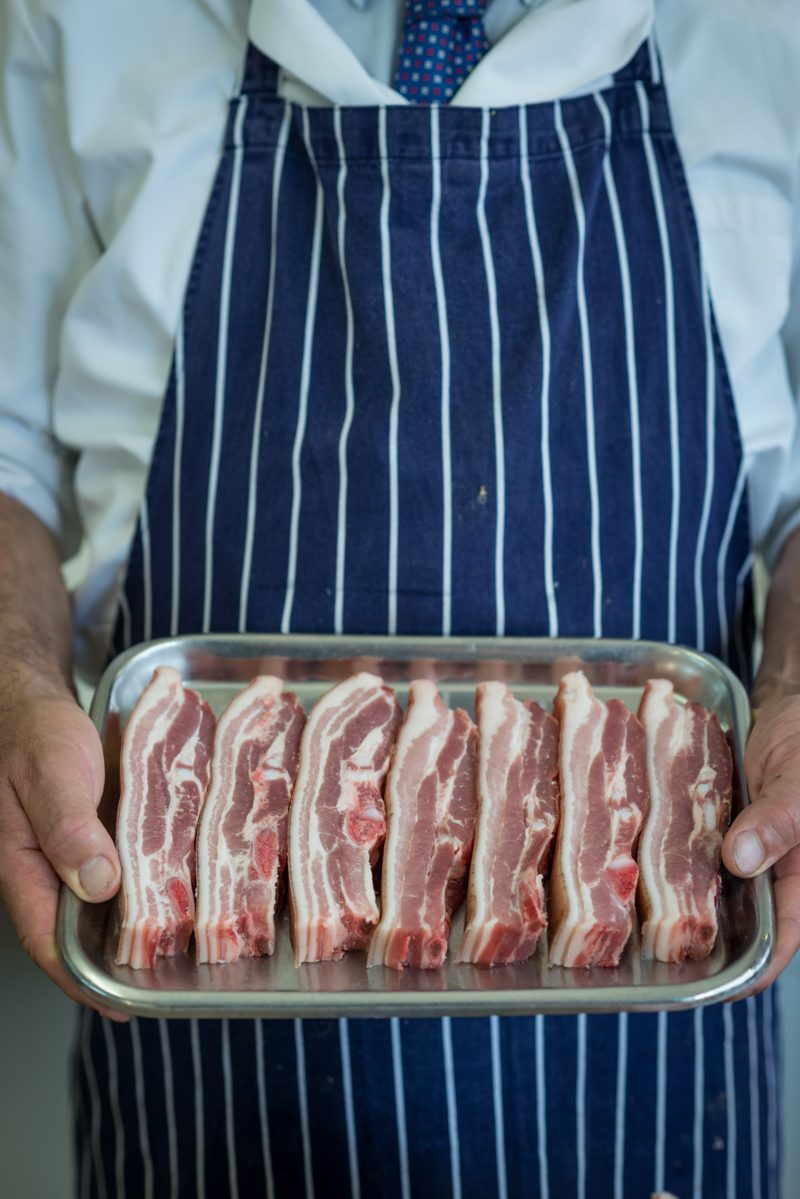 Butcher in blue and white apron with a tray of raw meat